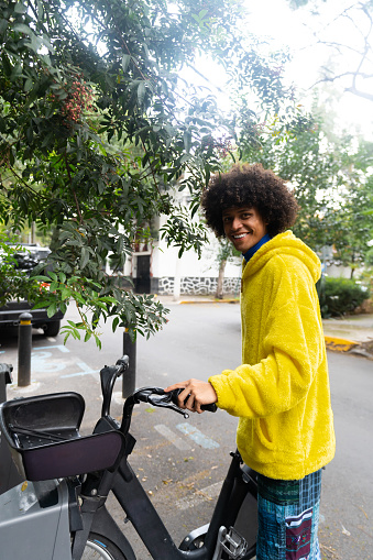 Young man afro mexican is taking a rental bike from the parking station lot