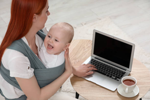 istock Mother using laptop while holding her child in sling (baby carrier) indoors 1709001618