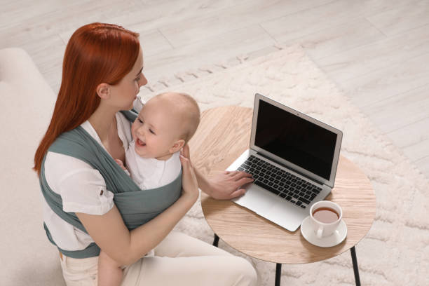 istock Mother using laptop while holding her child in sling (baby carrier) indoors 1709002662