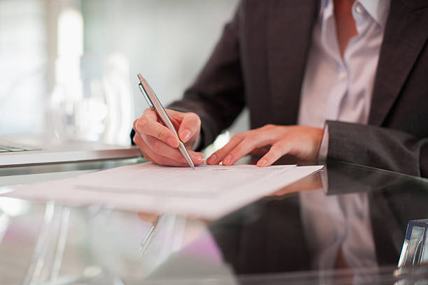 businesswoman writing on paper at desk - สัญญา เอกสาร ภาพสต็อก ภาพถ่ายและ��รูปภาพปลอดค่าลิขสิทธิ์