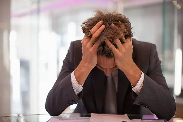 Photo of Frustrated businessman sitting at desk with  head in hands