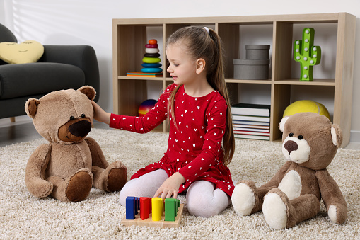 Cute little girl playing with teddy bears and cubes at home