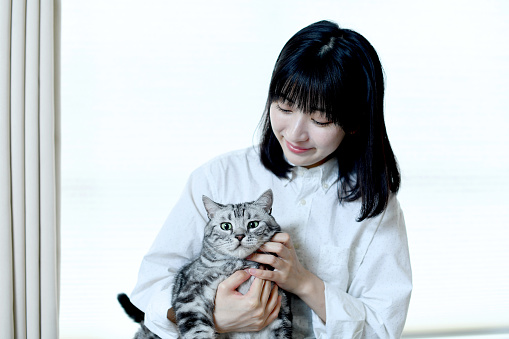 Smiling young Asian woman holding a pet (cat) and having skinship indoors