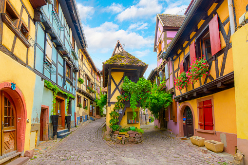 A picturesque fork in the road surrounded by half-timbered medieval homes in the idyllic picturesque village of Eguisheim, France, in the Alsace region. Eguisheim is a medieval village in France’s Alsace wine region. The narrow, concentric streets of its old town are lined with many preserved half-timbered houses.