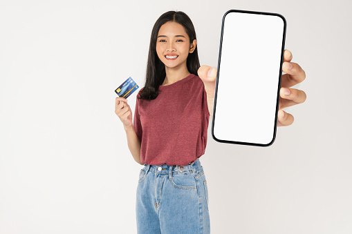 Happy young Asian woman holding smartphone with credit card win on white background.