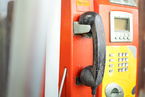 The antique analog payphone or telephone box, close-up and selective focus at handset. Vintage technology and equipment object photo.