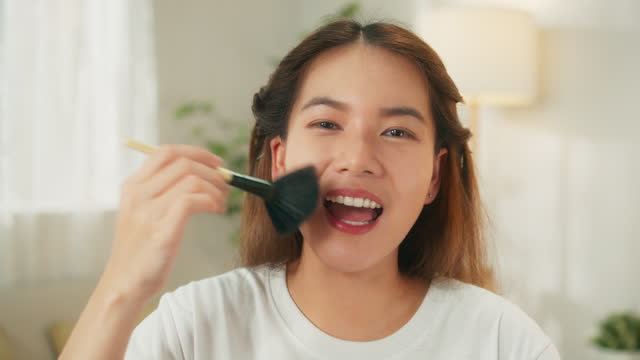 beautiful young Asian woman applying makeup, enhancing her beauty at table filled with cosmetics, beauty routine at home concept.