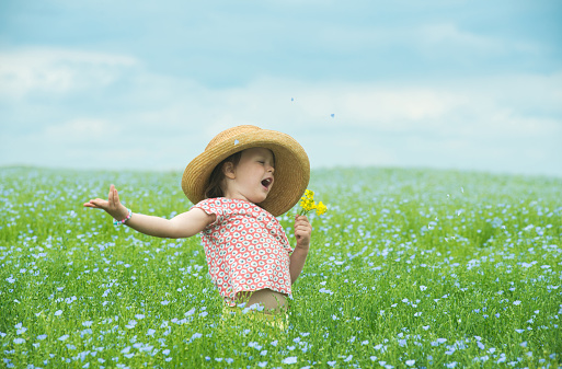 Adorable child singing in a straw hat with a bouquet of yellow flowers in the middle of a beautiful field of flowers.