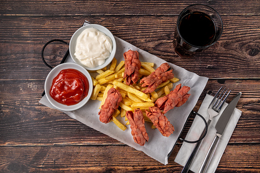 French fries and deep fried sausage with ketchup and mayonnaise on wooden table