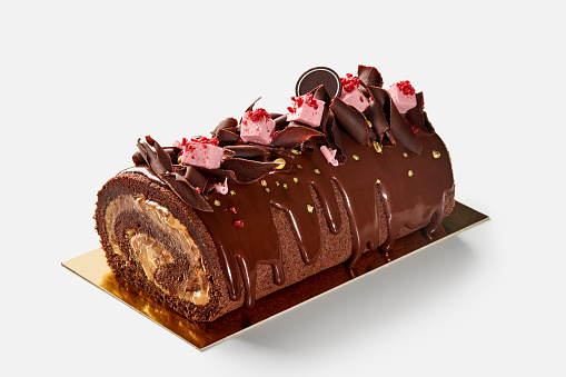 Delicious sweet soft chocolate sponge cake roll with filling of condensed milk buttercream topped with ganache, dark chocolate chips and berry marshmallow served on golden cardboard