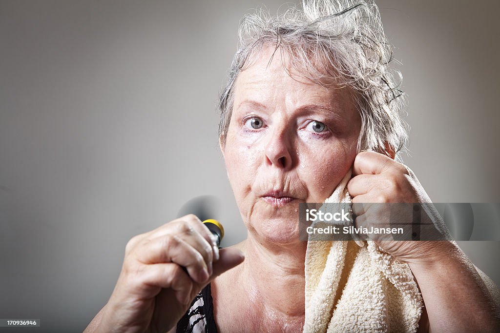 mature woman having hot flash woman in her fifties sweatening,  having hot flashes and trying to cool with small fan, drying face with towel Menopause Stock Photo