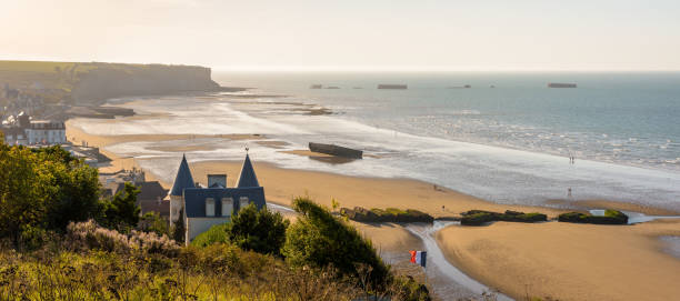Arromanches-les-Bains, France - Sept. 4, 2023: Panoramic view over Arromanches beach at sunset, with remains of the WWII Mulberry harbor lying on the sand and the Phoenix caissons in the sea.