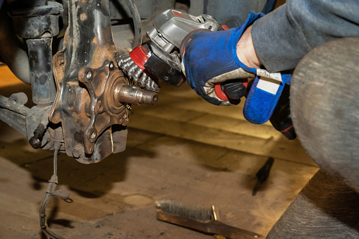 The car mechanic cleans, derusts and maintains the rear hub bearing with ginding machine in the garage. Workshop. Auto service. Protective gloves.