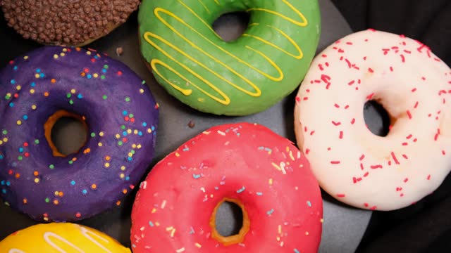 Close up, colorful donuts with cream various confectionery glaze and sprinkles on black plate background rotate.