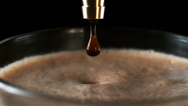 Slow motion close up shot of a drops of a black coffee falling into a cup