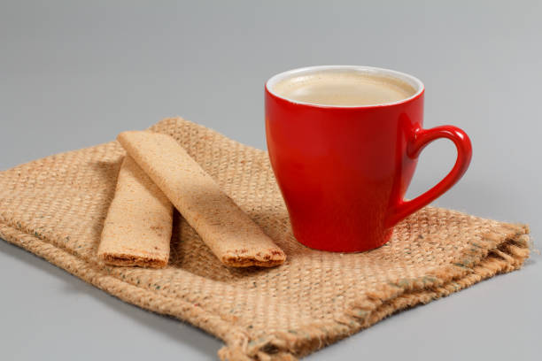 Red cup of black coffee and some kind of pastries on the sackcloth bag.