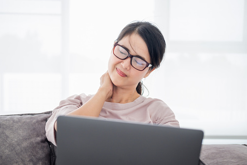 Office syndrome concept. mature middle age asian woman feeling pain in neck and shoulder after working on computer laptop for a long time. She stretches to relax her muscles