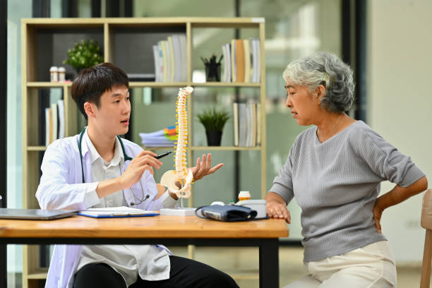 Orthopedist giving consultation about scoliosis or spinal problems to mature female patient during medical exam stock photo