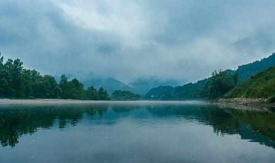 Mountains hiding in low clouds and a pair of fishermen on the bank of a fog-covered river