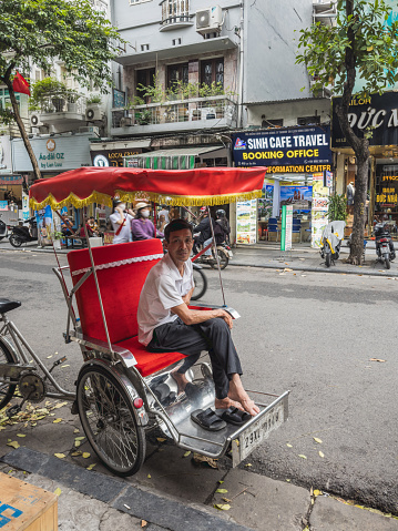A local driver waits for passengers on his tuk-tuk on a city street. Hanoi, Vietnam - September 4, 2023.