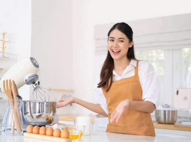 istock Homemade authentic hobby baking. Smiling young woman in white kitchen. Table with ingredients and accessories for homemade baked goods. Flour, sugar, eggs, butter, honey, bowl, whisk, rolling pin. 1709493826