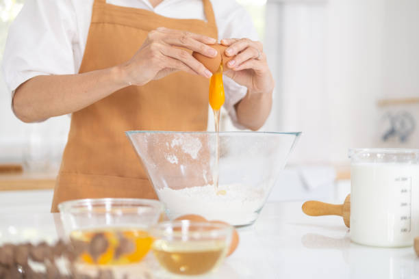 istock Close-up front view footage, a female cook in light brown apron is cracking an egg into a cup to prepare a meal on white table in the home's kitchen. Eating egg yolks is a healthy breakfast. 1709497104