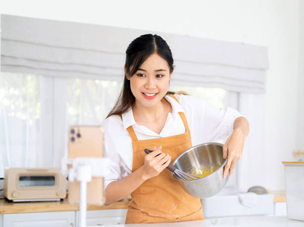 istock baker online courses. food preparing and culinary training class concept. smiling asian chef mixing flour in the kitchen and shooting video of herself using mobile phone on a tripod. 1709501483