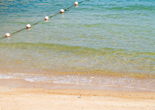 Clear emerald green sea with white foam and yellow sand on the beach with human footprints