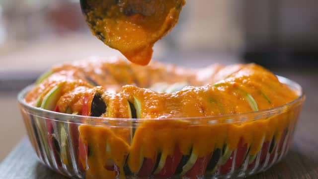Sliced vegetables in the glass bowl are poured with sauce. Ratatouille dish cooking preparation