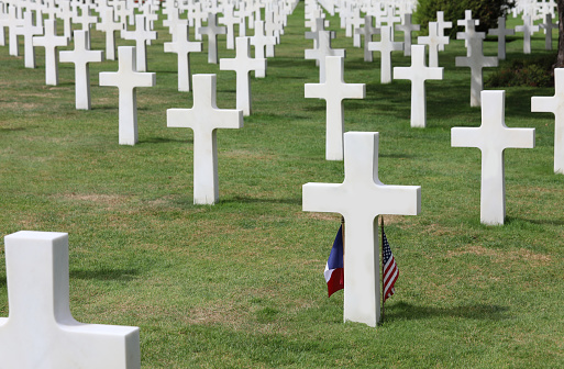 Colleville-sur-Mer, FRA, France - August 21, 2022: American Military Cmemetry with crosses on graves and flags of USA and France on graves of soldiers