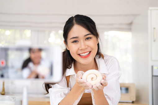 Portrait of smiling professional beauty asian woman chef having fun cooking with dough for homemade bake cookie and cake ingredient on table in kitchen. Indoor studio shot on kitchen background.