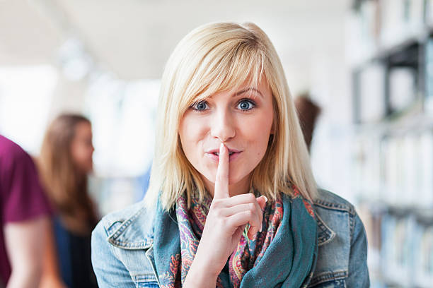 Silence Please Teenage girl in a library putting finger on her lips. finger on lips stock pictures, royalty-free photos & images