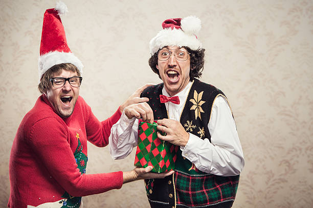 Christmas Sweater Nerds Two goofy looking men in ugly looking Christmas cardigans and sweaters (complete with matching red bow tie and a classy mustache).  One man opens a gift that his friend has given him.  Damask style vintage wall paper in the background.  Horizontal with copy space. christmas ugliness sweater nerd stock pictures, royalty-free photos & images