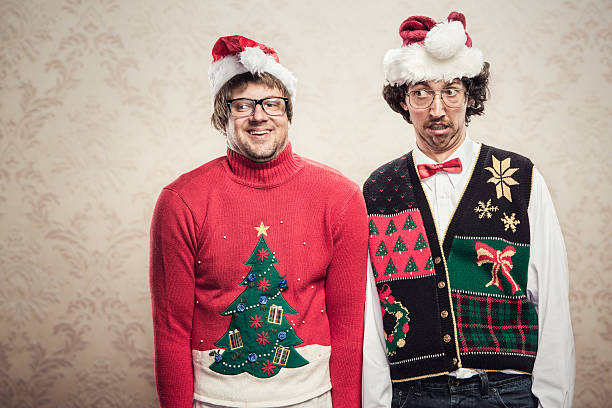 Christmas Sweater Nerds Two goofy looking men in ugly looking Christmas cardigans and sweaters (complete with matching red bow tie and a classy mustache) stand looking awkward for a holiday photo.  Damask style vintage wall paper in the background.  Horizontal with copy space. sweater stock pictures, royalty-free photos & images