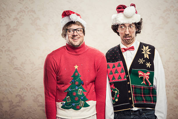 Christmas Sweater Nerds Two goofy looking men in ugly looking Christmas cardigans and sweaters (complete with matching red bow tie and a classy mustache) stand looking awkward for a holiday photo.  Damask style vintage wall paper in the background.  Horizontal with copy space. christmas nerd sweater cardigan stock pictures, royalty-free photos & images