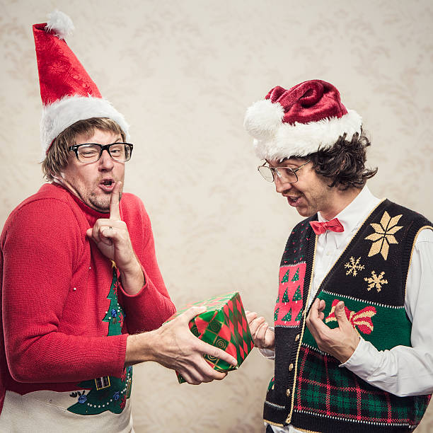 Christmas Sweater Nerds Two goofy looking men in ugly looking Christmas cardigans and sweaters (complete with matching red bow tie and a classy mustache).  One man opens a gift that his friend has given him.  Damask style vintage wall paper in the background.  Horizontal with copy space. christmas ugliness sweater nerd stock pictures, royalty-free photos & images