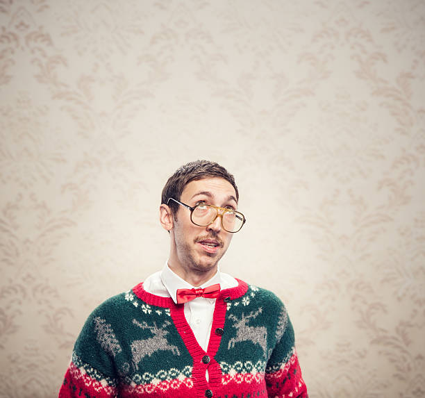 Christmas Sweater Nerd A man in a knit reindeer Christmas cardigan button up sweater, complete with matching red bow tie and a classy mustache.  He looks up as if he is thinking or planning something.  Copy space room above his head for whatever he's "looking at".  Damask style vintage wall paper in the background.  Square with copy space. kitsch photos stock pictures, royalty-free photos & images
