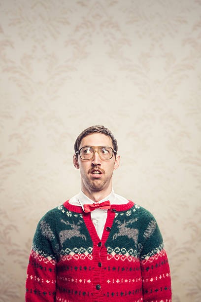 Christmas Sweater Nerd A man in a knit reindeer Christmas cardigan button up sweater, complete with matching red bow tie and a classy mustache.  He looks like he is confused as he thinks about something.  Damask style vintage wall paper in the background.  Vertical with copy space. nerd sweater stock pictures, royalty-free photos & images