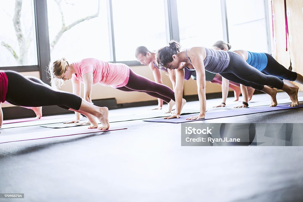 Group Yoga Class in Studio A mixed ethnicity group of men and woman practice different yoga forms and positions in a bright well lit studio.  Here they are in plank pose, or Uttihita Chaturanga Dandasana.  Horizontal with copy space. Active Lifestyle Stock Photo