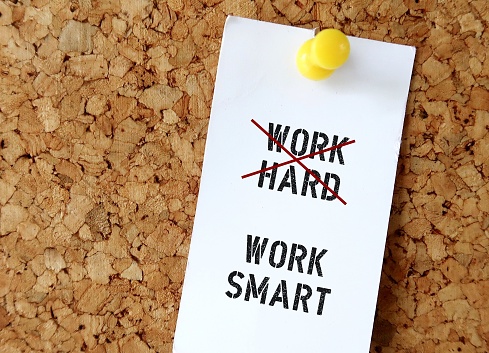 Pinned note on board with text WORK HARD (red crossing) WORK SMART , means smart worker complete work within timelines using shortcut ,proper planning , prior research , instead of working long hours