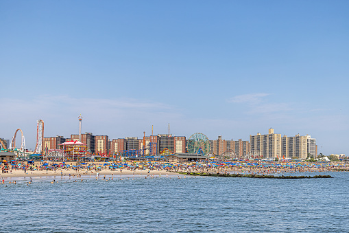 Coney Island, New York, USA - August 20th 2023:  Residential buildings behind a crowded public beach with many people on a sunny day