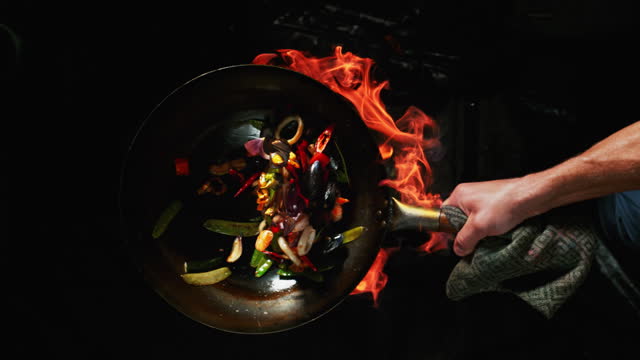Skilled cook flipping fried vegetables in a wok
