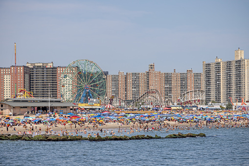 Coney Island, New York, USA - August 20th 2023:  Residential buildings behind a crowded public beach with many people on a sunny day