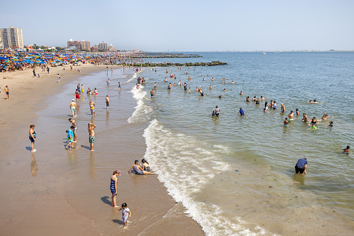 Coney Island, New York, USA - August 20th 2023:  People enjoying the cooling Atlantic ocean from the sandy beach