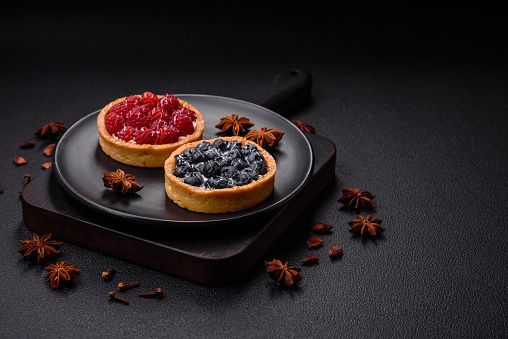 Delicious fresh sweet round tart with ripe blueberries and cream on a dark concrete background