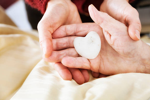 2 hands holding a hand of senior adult, 89 years old, in hospital holding stone in heart shape