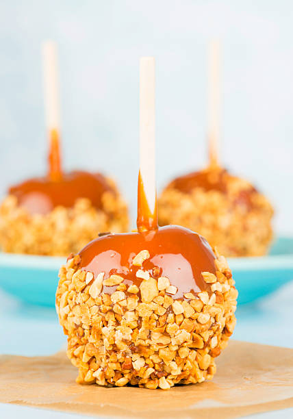 Candy Apples Single candy apple on parchment paper with defocused candy apples in background caramel apple stock pictures, royalty-free photos & images