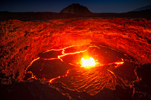 View from the crater rim of Erta Ale - one of the most active vulancoes in the world - into the active, red glowing lava lake. Erta Ale is a continuously active basaltic shield volcano in the Afar Region of northeastern Ethiopia, only some kilometers from the border to Eritrea.