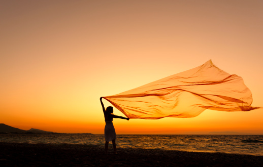 woman silhouette on beach at sunset with flying scarf.