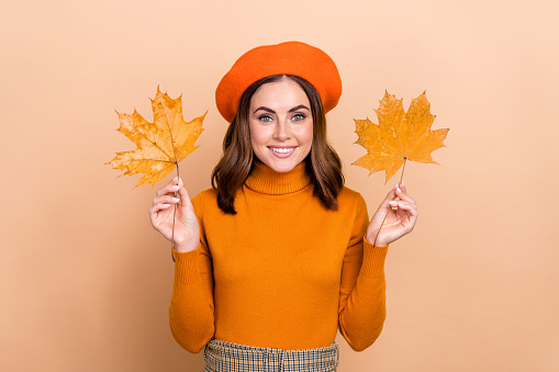 Photo of cheerful pretty lovely lady wear stylish clothes showing leaves rejoice october weather time isolated on beige color background.